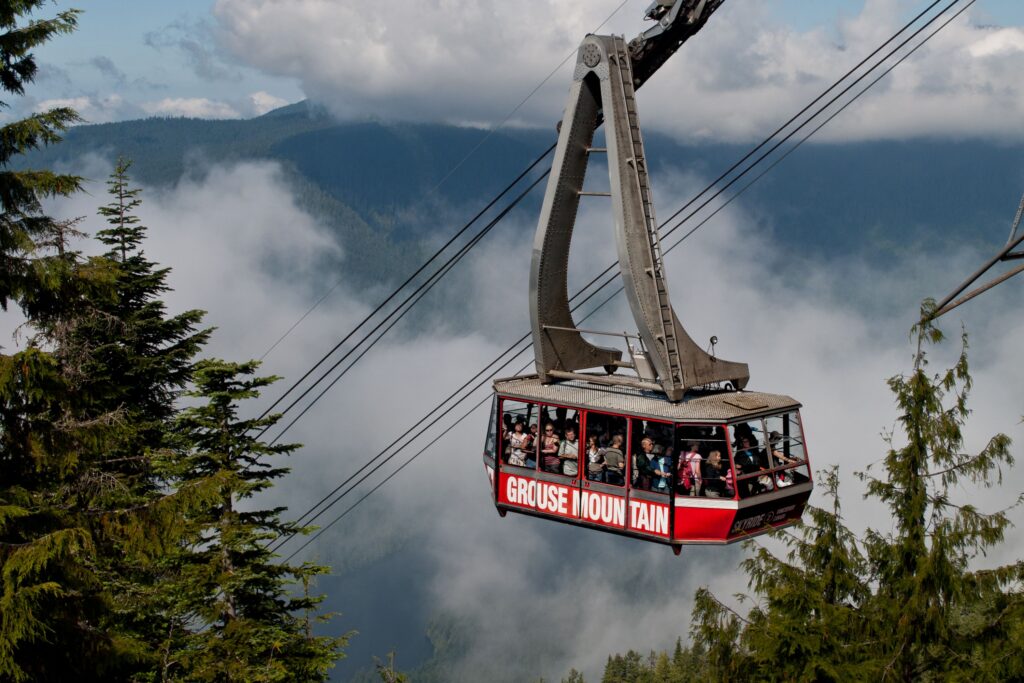 Visitors riding the Grouse Mountain Skyride cable car above the forest with panoramic mountain views in North Vancouver, Canada.