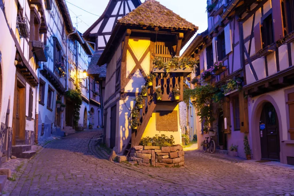Traditional half-timbered houses surrounding a cobblestone street in a picturesque Alsatian village at dusk