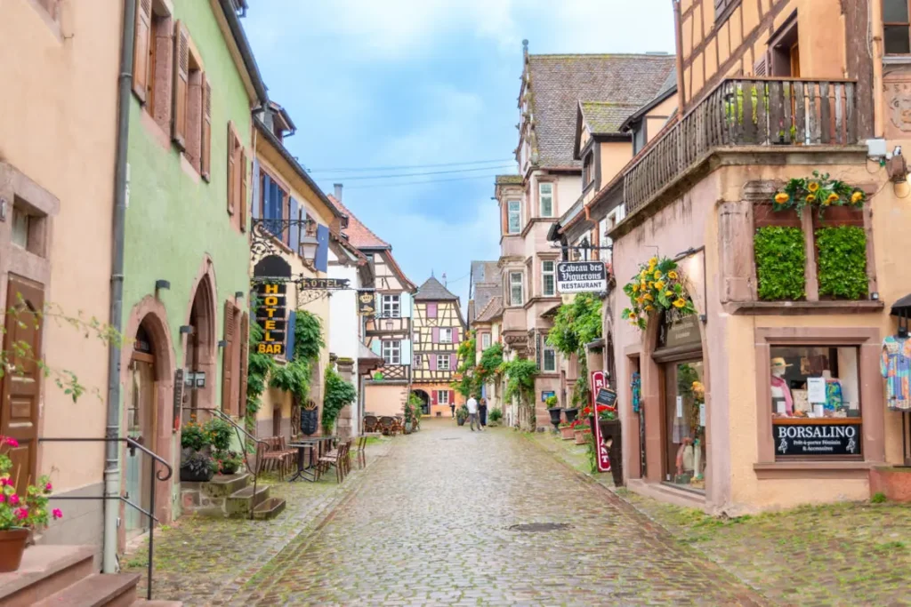 Charming cobblestone street lined with pastel-colored houses, traditional Alsatian architecture and flower-filled balconies