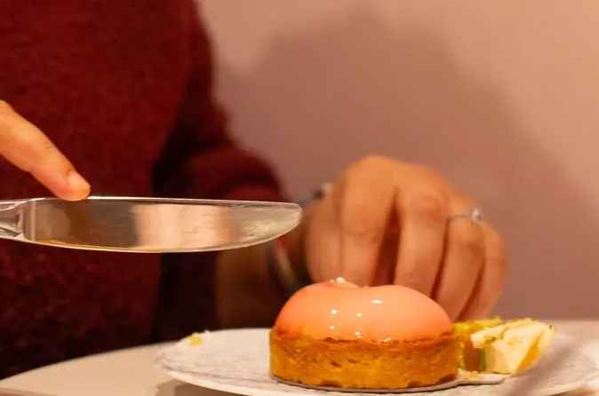 Person preparing to taste a small French dessert topped with glossy pink icing during a culinary experience