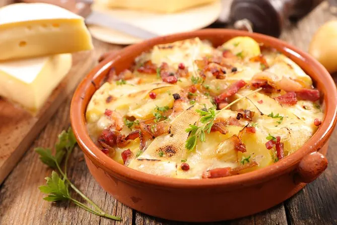 Traditional Savoyard tartiflette with melted cheese, potatoes and bacon served in a rustic ceramic dish