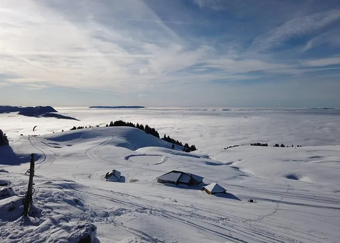 Snow-covered Alpine hills and mountain cabins above a sea of clouds near Annecy in winter