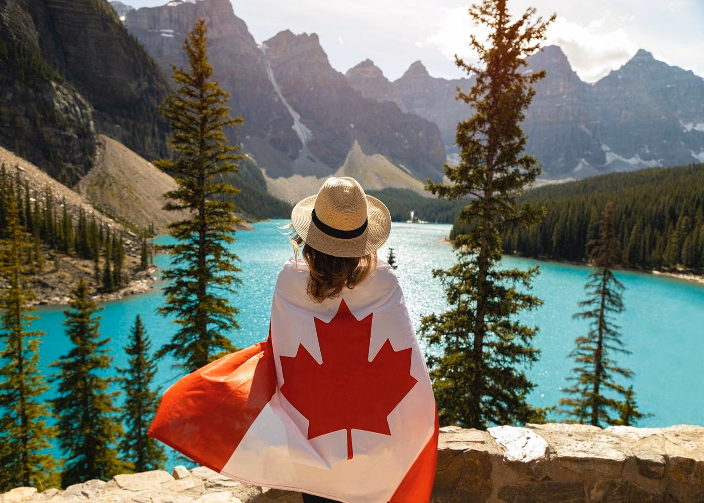 Traveler wrapped in a Canadian flag overlooking the turquoise waters of Moraine Lake in Banff National Park