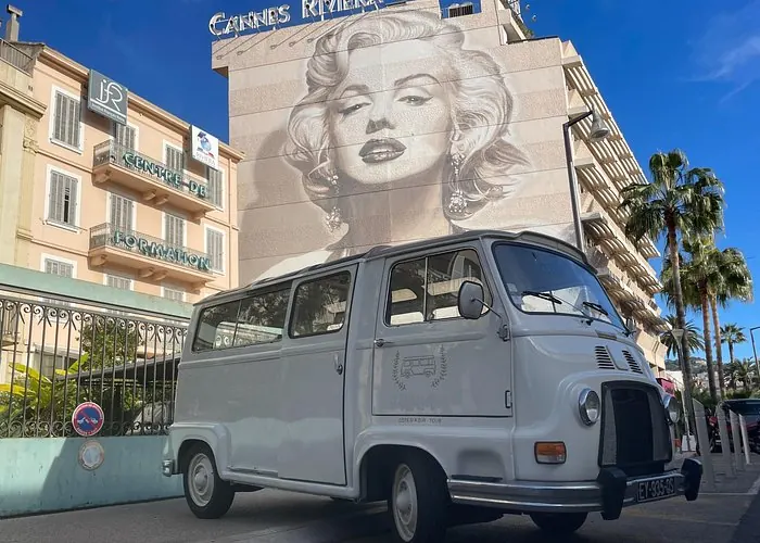 Classic French vintage sightseeing bus parked in Cannes in front of a large Marilyn Monroe mural