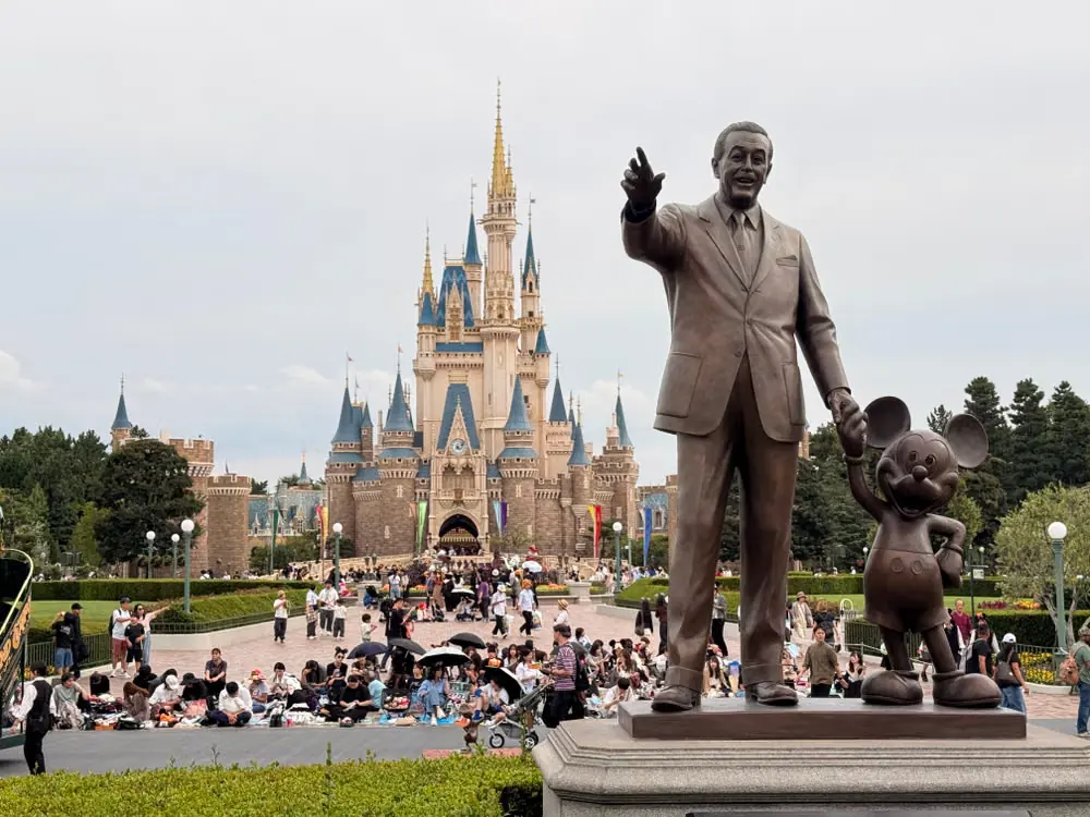 Walt Disney and Mickey Mouse Partners statue with a fairytale castle in the background at a Disney theme park