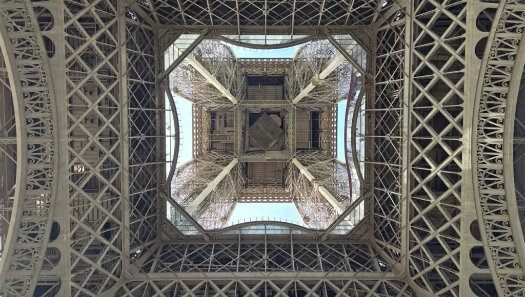 View looking up through the iron lattice structure beneath the Eiffel Tower in Paris