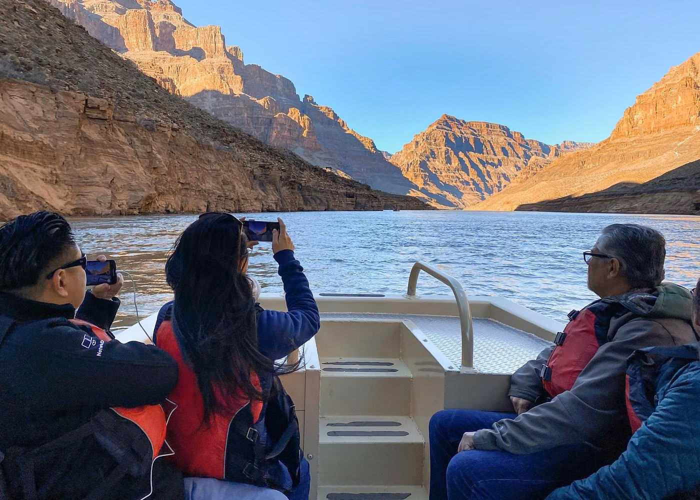 Tourists wearing life jackets on a boat exploring the Colorado River between towering Grand Canyon cliffs