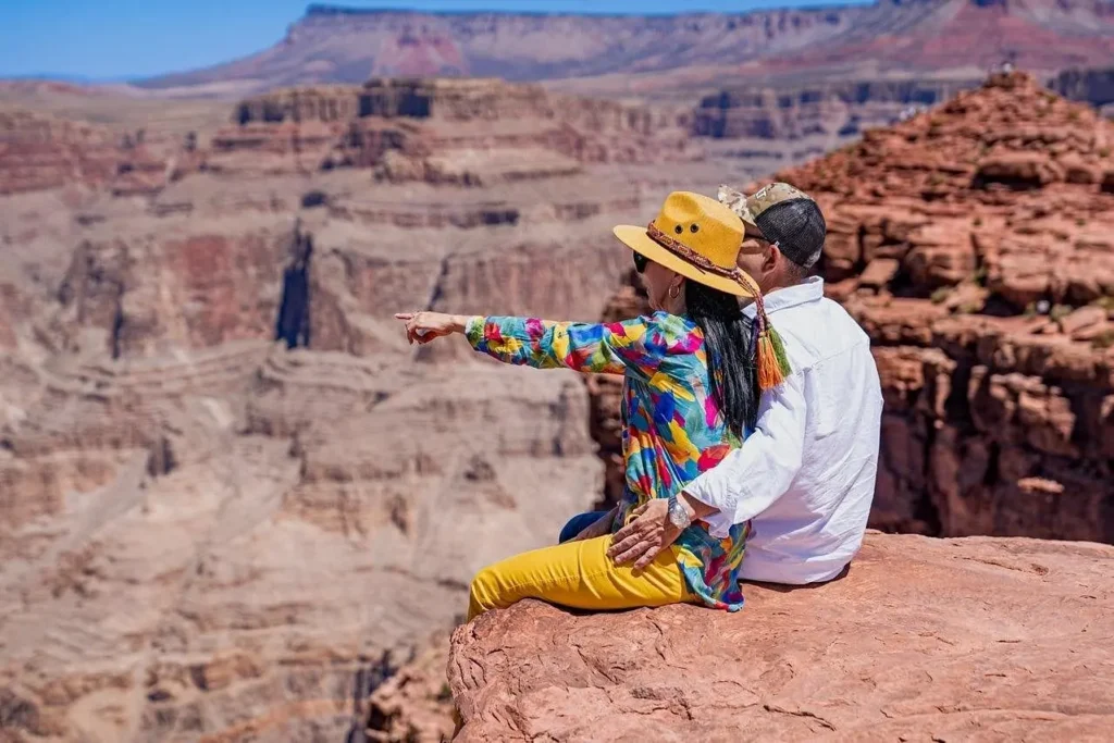 Couple sitting on a rocky viewpoint overlooking the dramatic red cliffs of the Grand Canyon