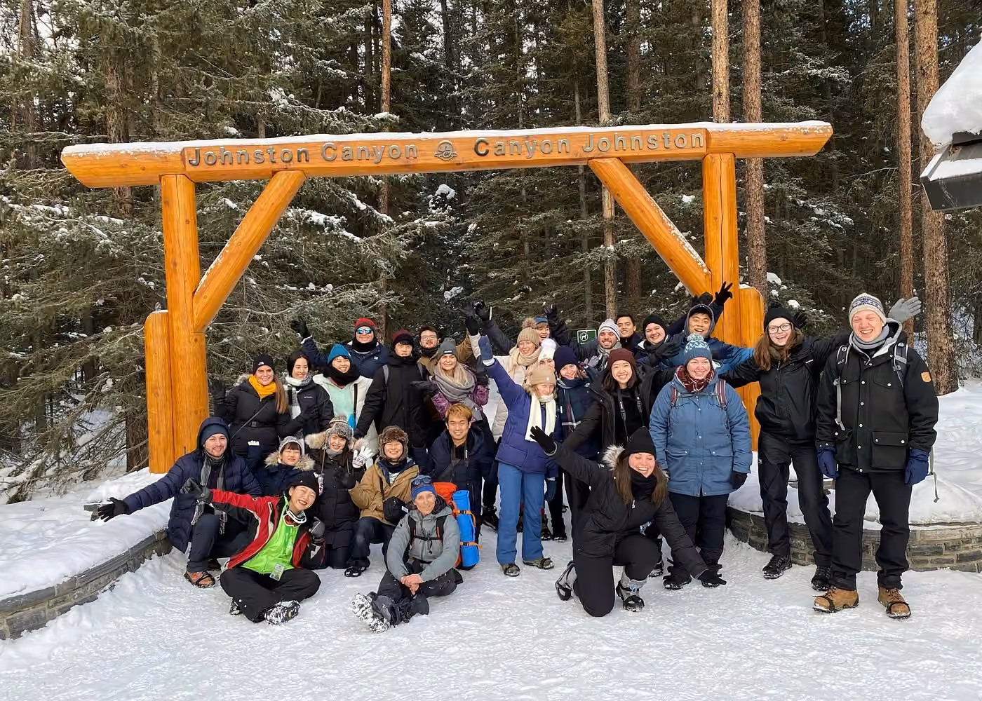 Group of visitors posing beneath the Johnston Canyon entrance sign during a winter icewalk in Banff National Park