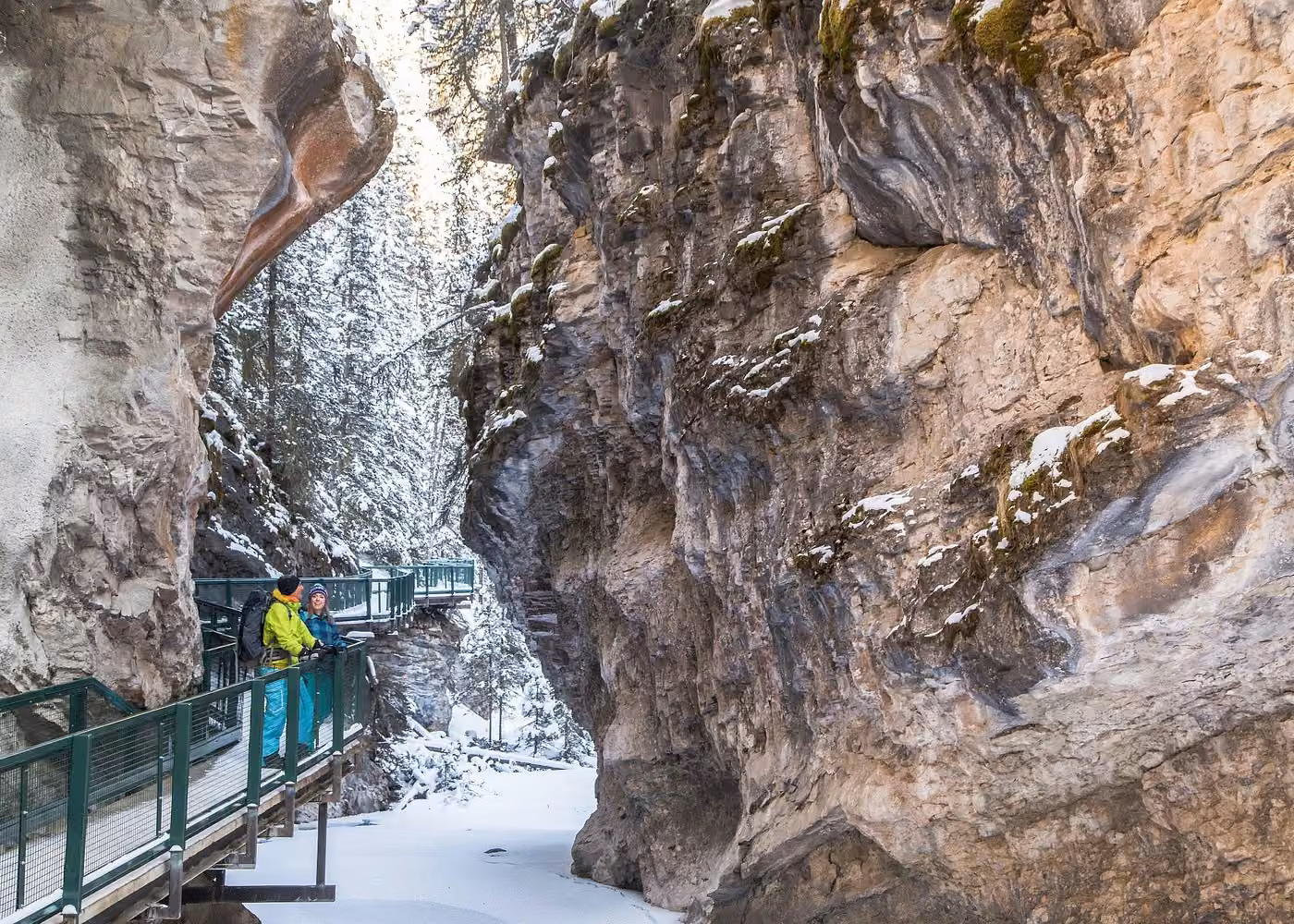 Visitors exploring the elevated Johnston Canyon walkway between snowy limestone cliffs in Banff National Park