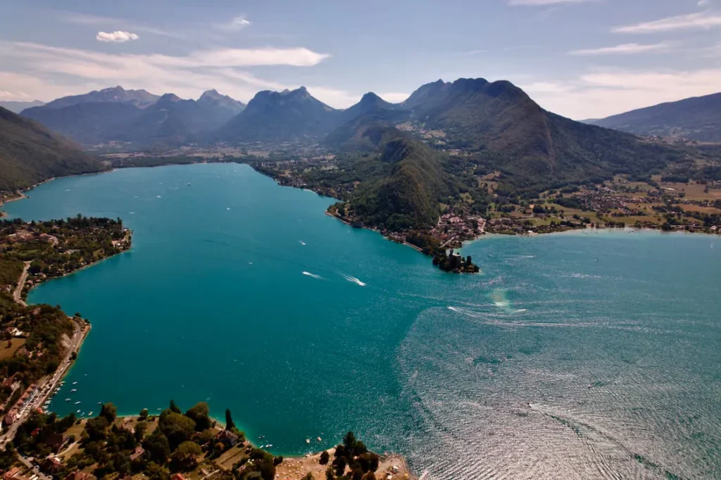 Aerial panoramic view of Lake Annecy and the surrounding French Alps, with turquoise water and green mountains