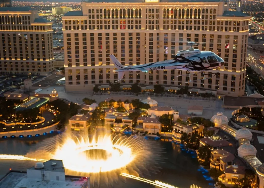Helicopter flying above the illuminated Bellagio fountains and hotel on the Las Vegas Strip at dusk
