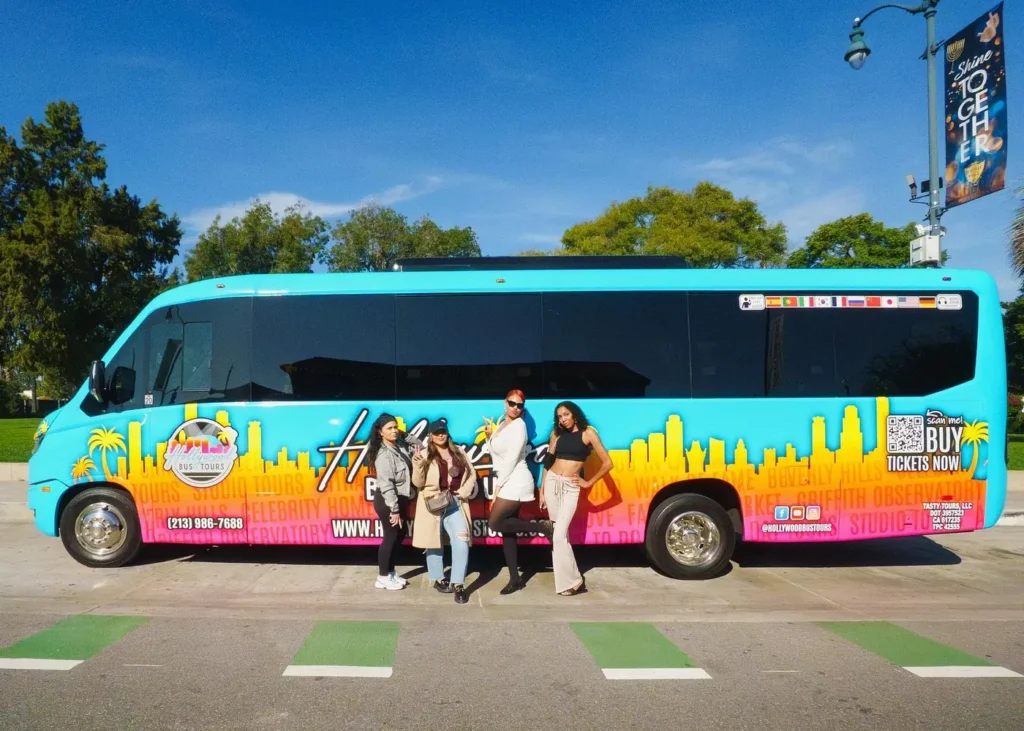 Travelers posing in front of a colorful Hollywood Bus Tours sightseeing bus in Los Angeles, California