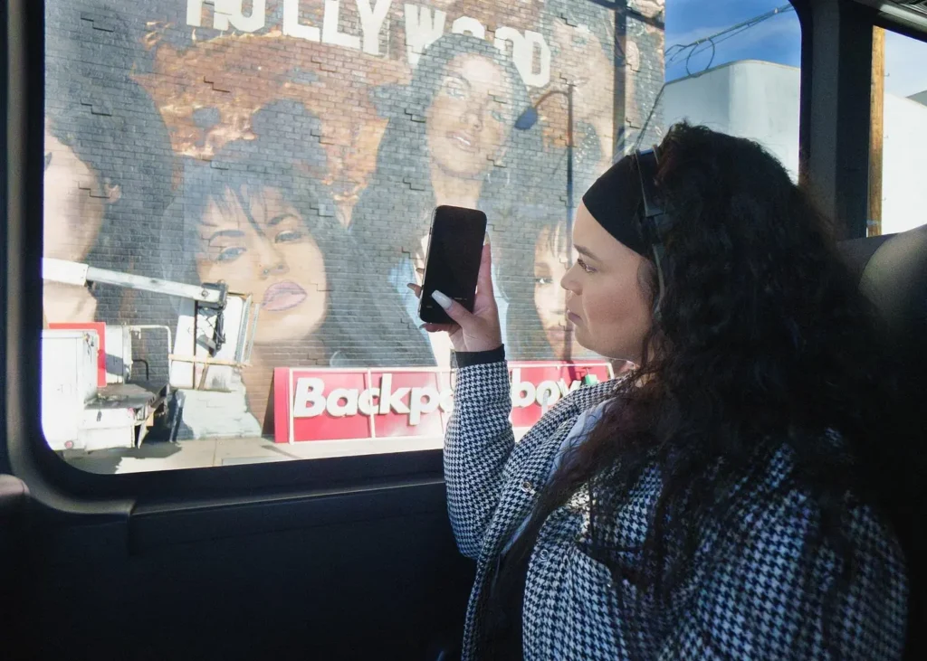 Tourist photographing a Hollywood celebrity mural through the window of a sightseeing bus in Los Angeles