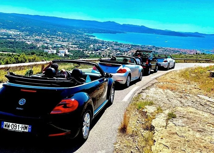 Convertible cars driving in convoy along a scenic coastal road overlooking the Mediterranean Sea