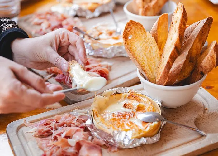 Baked creamy cheese served with cured ham and toasted bread during a French food tasting