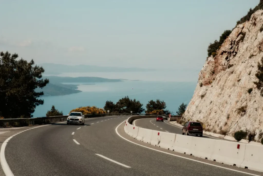 Winding coastal road overlooking the Mediterranean Sea with cars driving beside limestone cliffs