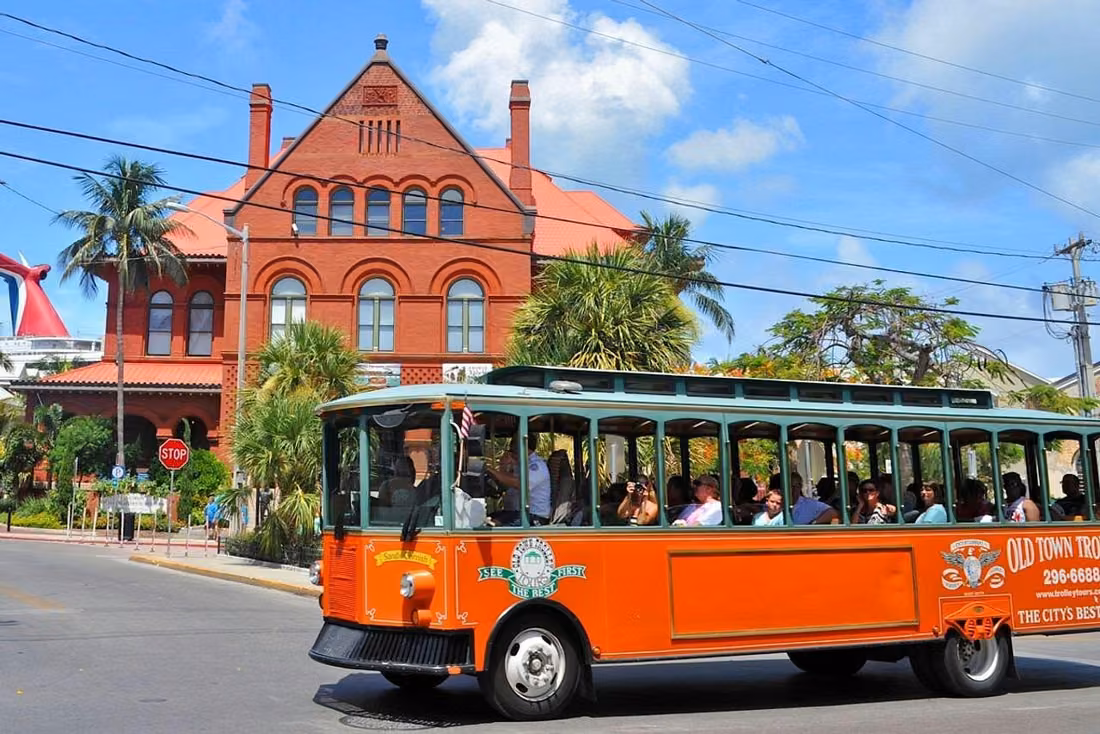 Orange Old Town Trolley sightseeing bus passing a historic red brick building and palm trees in Key West Florida