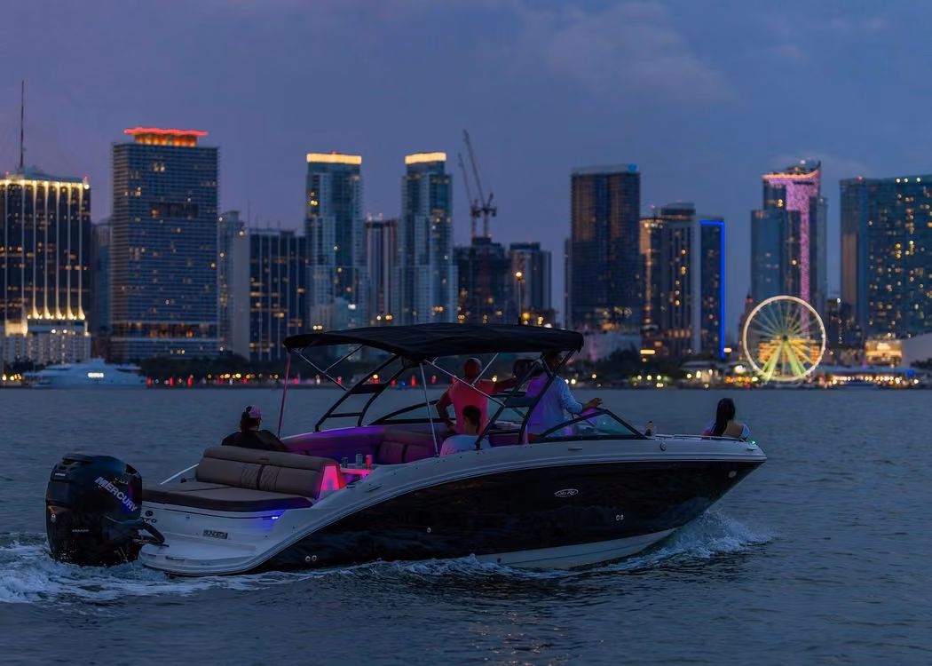 Private motorboat cruising on Biscayne Bay at dusk with illuminated Miami skyline and waterfront Ferris wheel