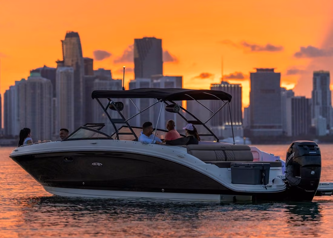 Private motorboat with passengers cruising at sunset against the Miami skyline and orange evening sky