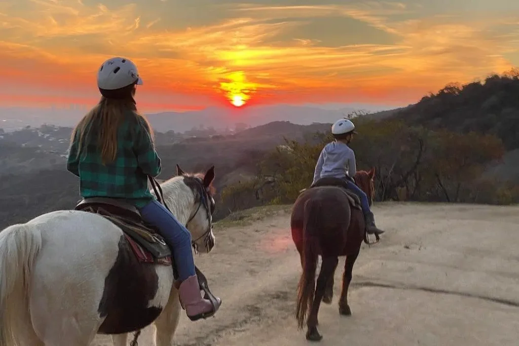 Two horseback riders wearing helmets overlooking a colorful sunset in the Hollywood Hills of Los Angeles