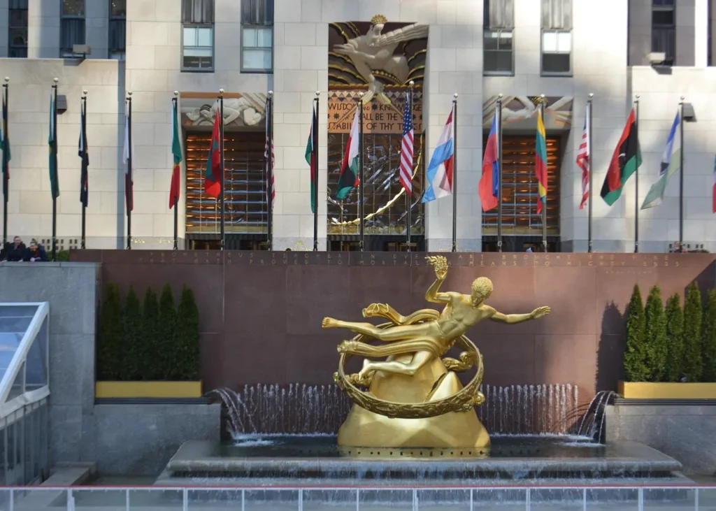 Golden Prometheus statue and fountain at Rockefeller Center in New York City, with international flags in the background