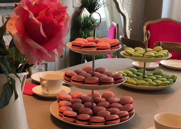 Pink, chocolate and green French macarons displayed on serving stands beside a rose and teacups