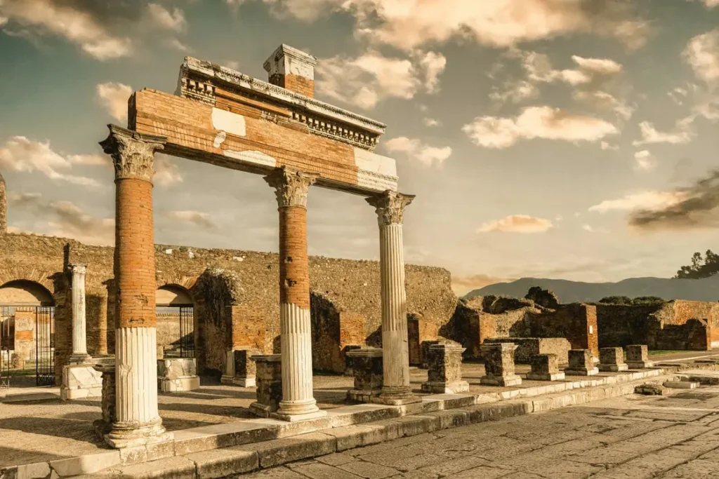 Ancient Roman columns and archaeological ruins at Pompeii, Italy, under a golden sky