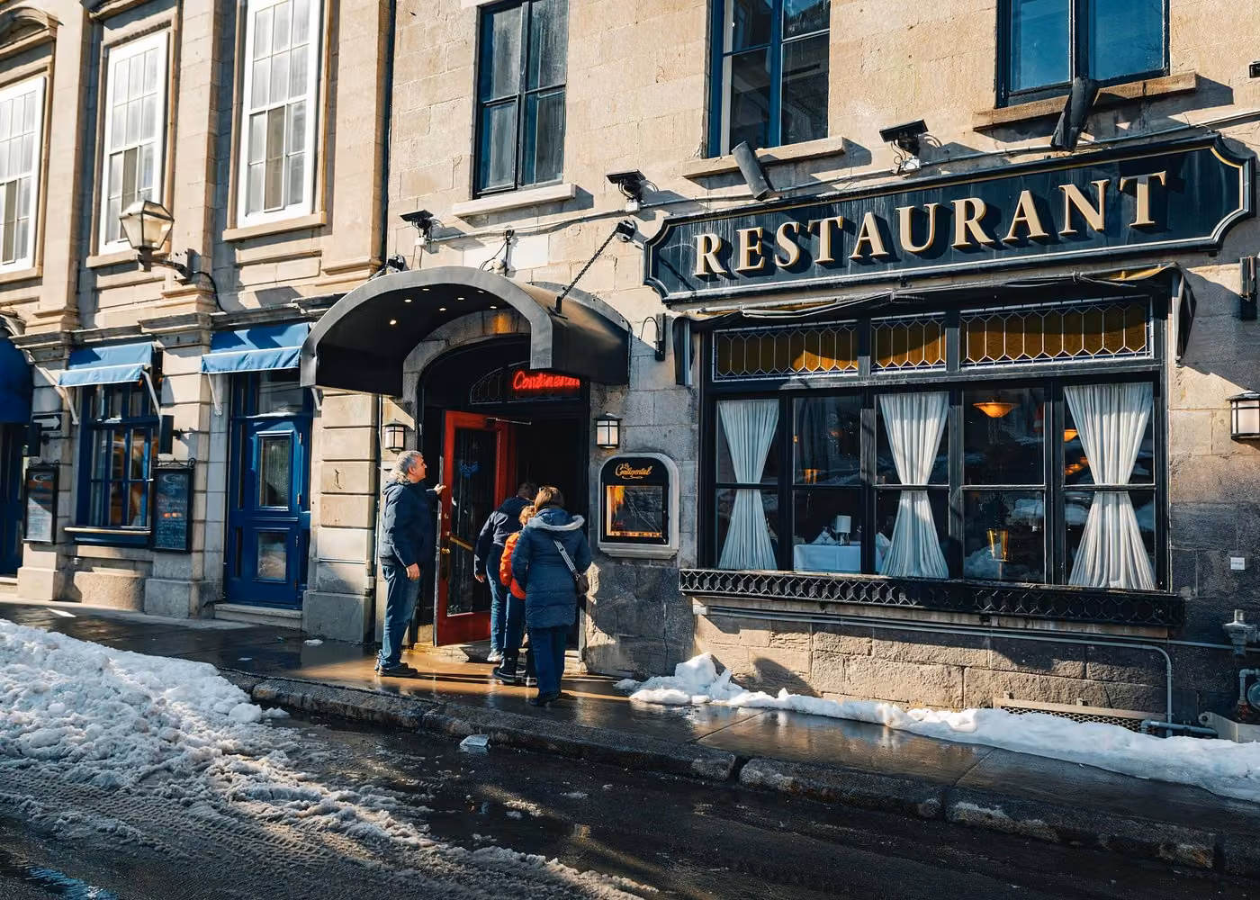 Historic restaurant entrance in Old Quebec City with visitors outside on a snowy winter day