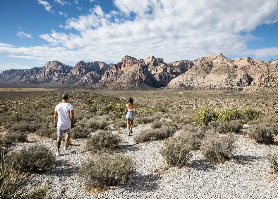 Two visitors walking through the desert landscape with rugged mountains in Red Rock Canyon near Las Vegas