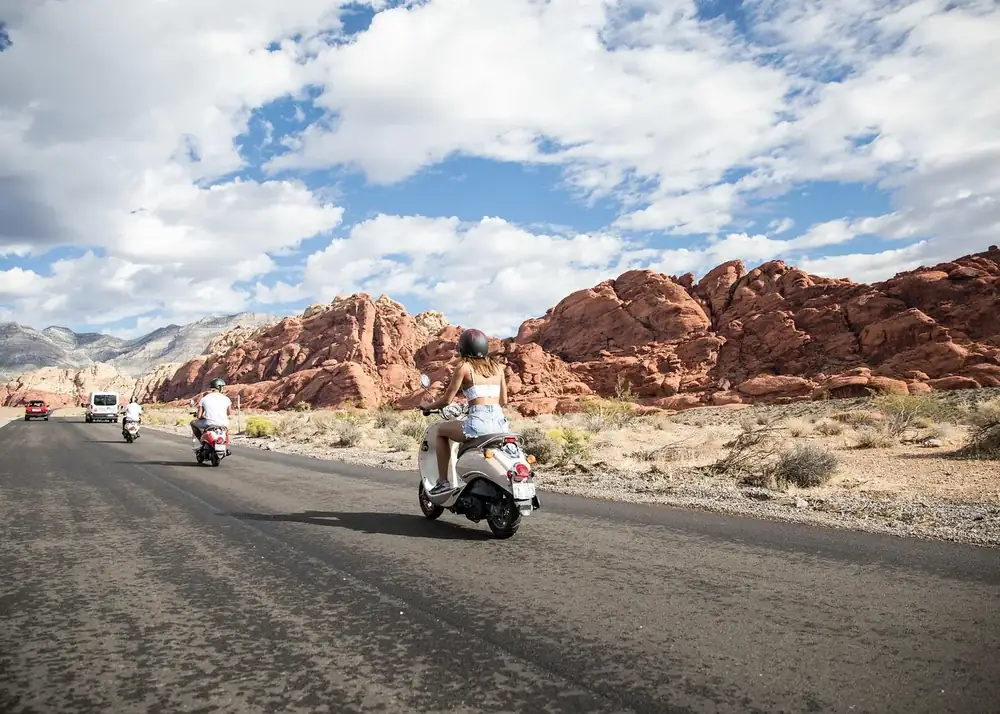 Tourists riding motor scooters along a scenic desert road surrounded by red sandstone formations in Red Rock Canyon Nevada