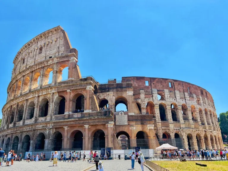 Exterior view of the Colosseum in Rome with ancient stone arches and visitors under a clear blue sky