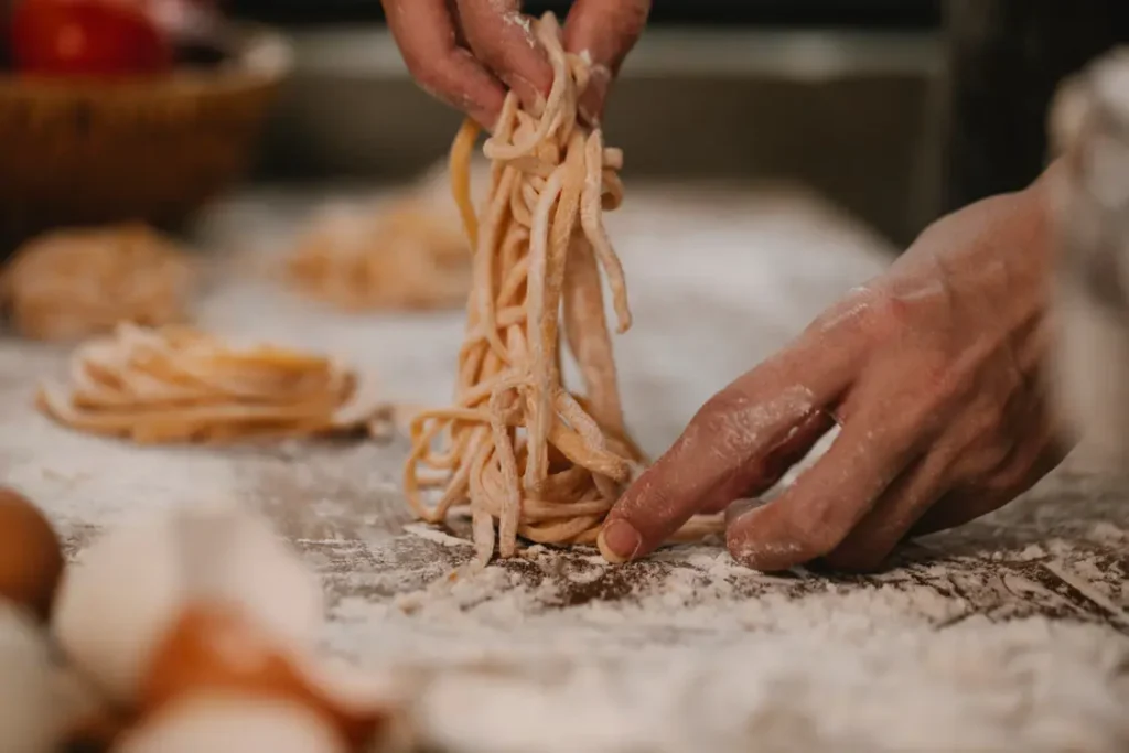 Hands preparing fresh fettuccine pasta on a floured table during an Italian cooking class