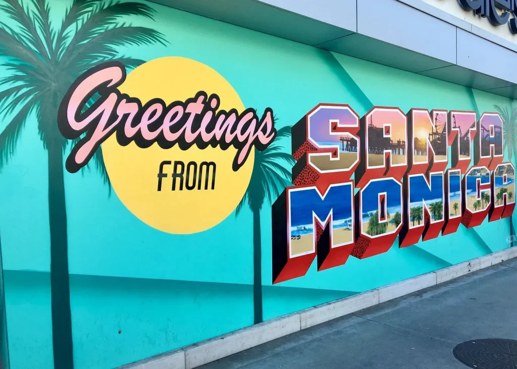 Colorful Greetings from Santa Monica mural with palm trees and beach-themed lettering in Santa Monica, California