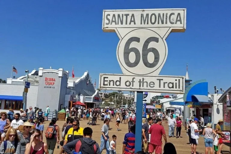Historic Route 66 End of the Trail sign overlooking crowds at Santa Monica Pier in California