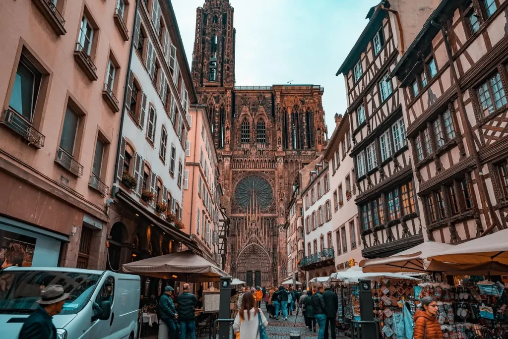 Strasbourg Cathedral seen from a cobblestone street lined with historic buildings, shops and pedestrians