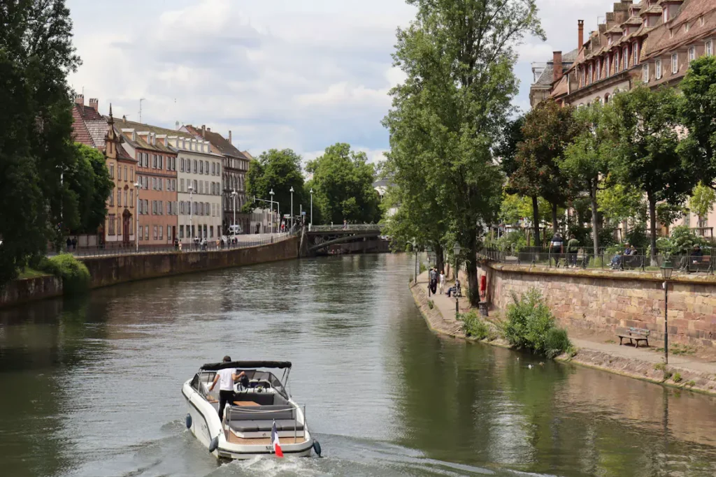 Private motorboat cruising along the River Ill between historic buildings and tree-lined banks in Strasbourg