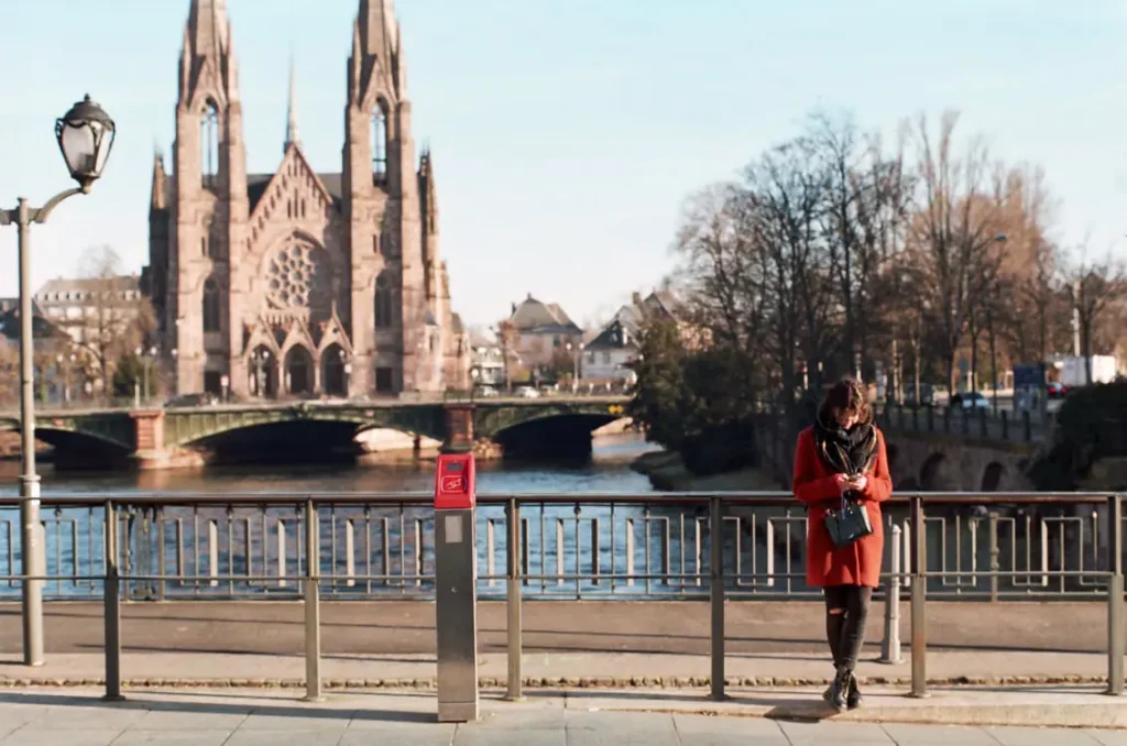 Woman standing beside the River Ill with Saint Paul's Church and a bridge in the background in Strasbourg