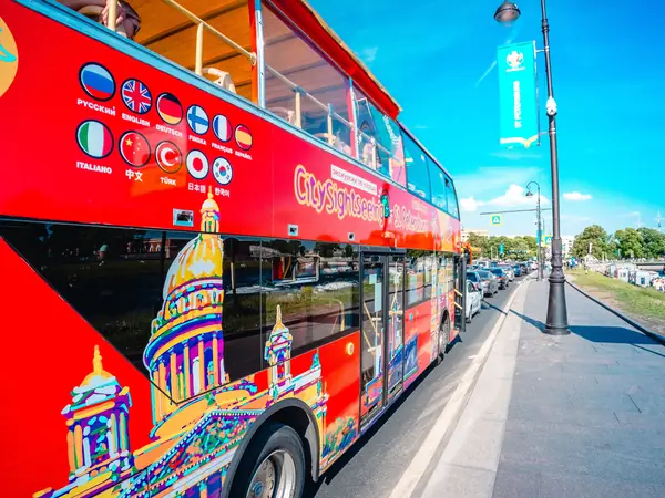 Red open-top sightseeing bus on a city street beside a waterfront
