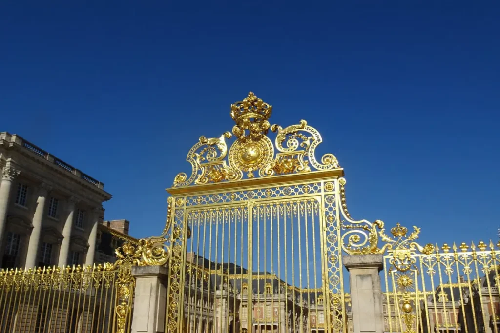 Ornate golden entrance gates of the Palace of Versailles beneath a clear blue sky
