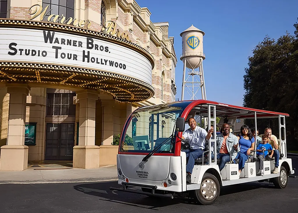 Warner Bros. Studio Tour Hollywood entrance with visitors aboard a guided tour tram and the famous WB water tower in Burbank