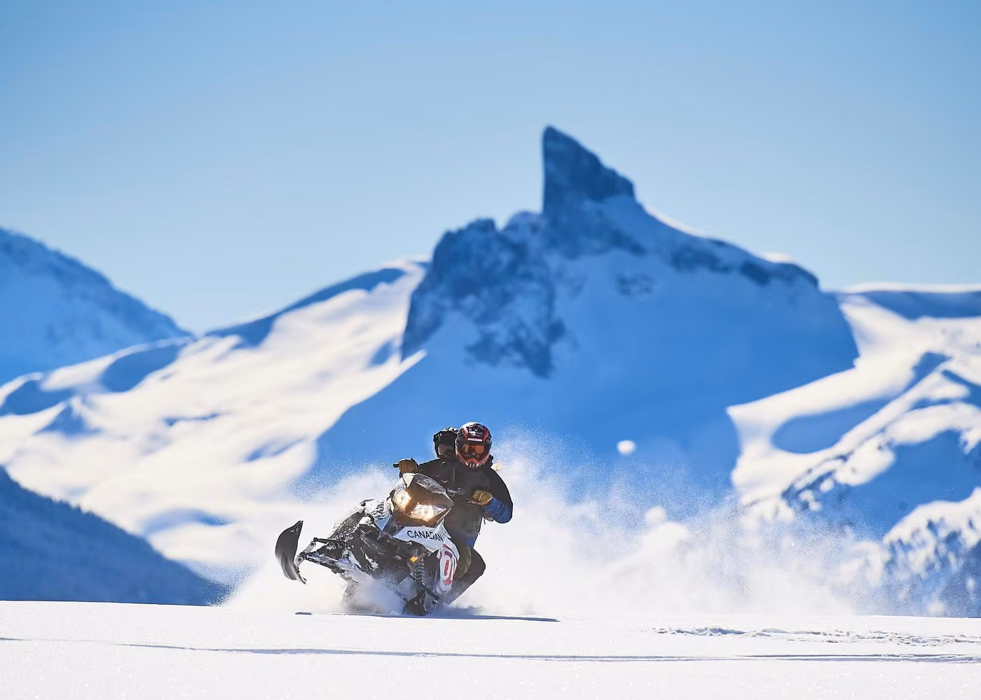 Snowmobile rider crossing a snowy alpine landscape with dramatic mountain peaks near Whistler, British Columbia