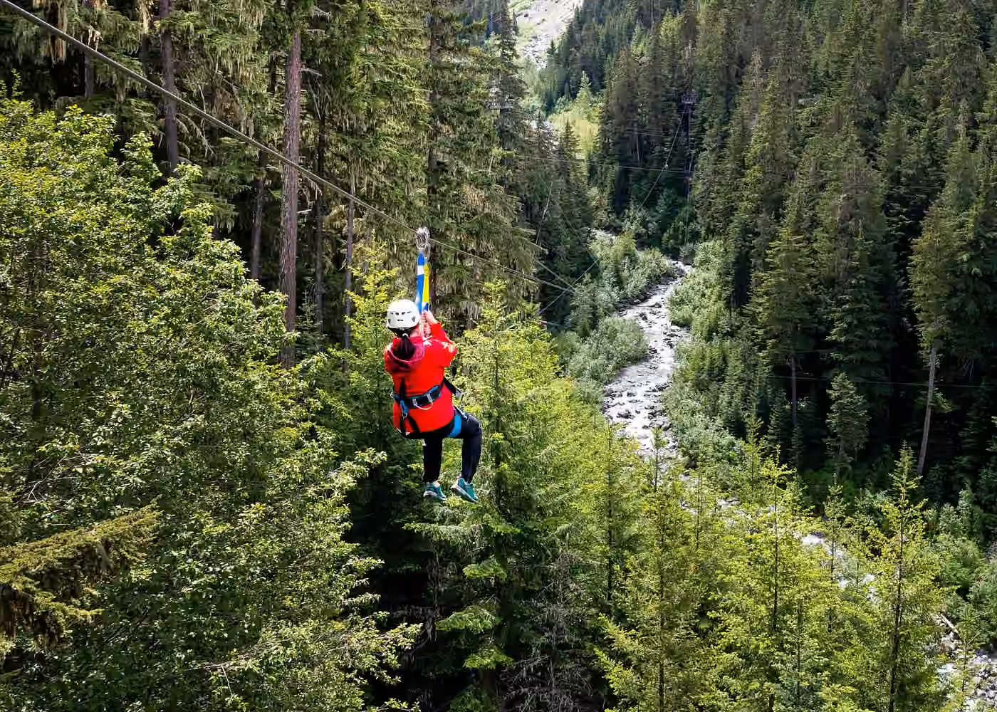 Person ziplining above a lush forest and mountain river during a Whistler zipline adventure in British Columbia
