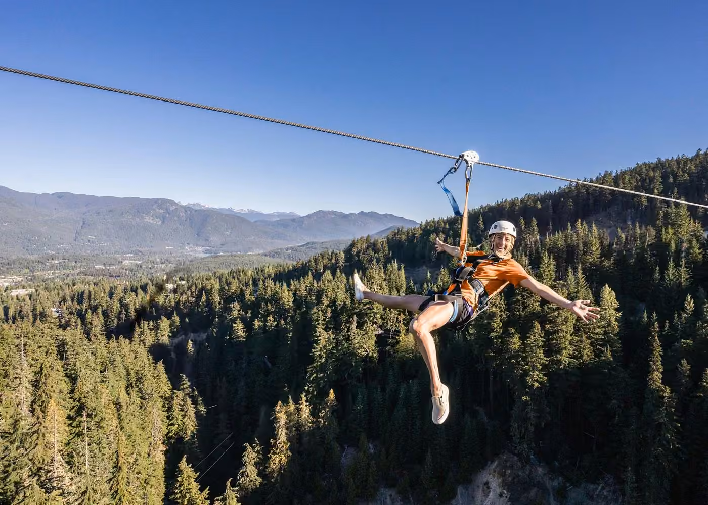 Woman ziplining above evergreen forests and mountain scenery in Whistler, British Columbia